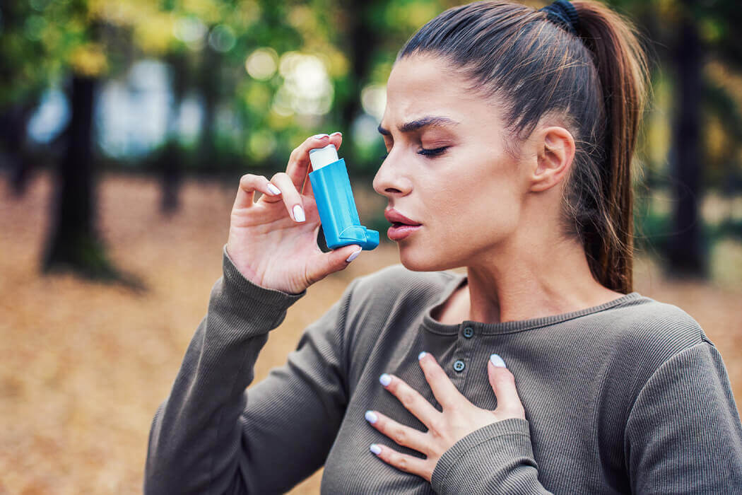 Woman with asthma clutching her chest while holding an inhaler up to her mouth.