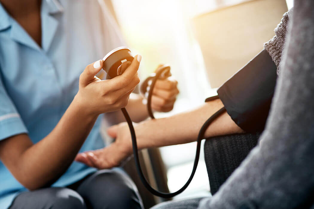 Arm laid out with a blood pressure cuff and the waist-down view of a doctor checking blood pressure.