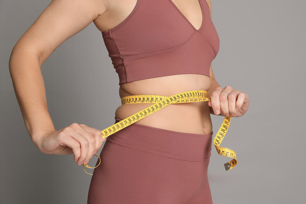 Woman wearing an activewear set with a measuring tape wrapped around her waist.