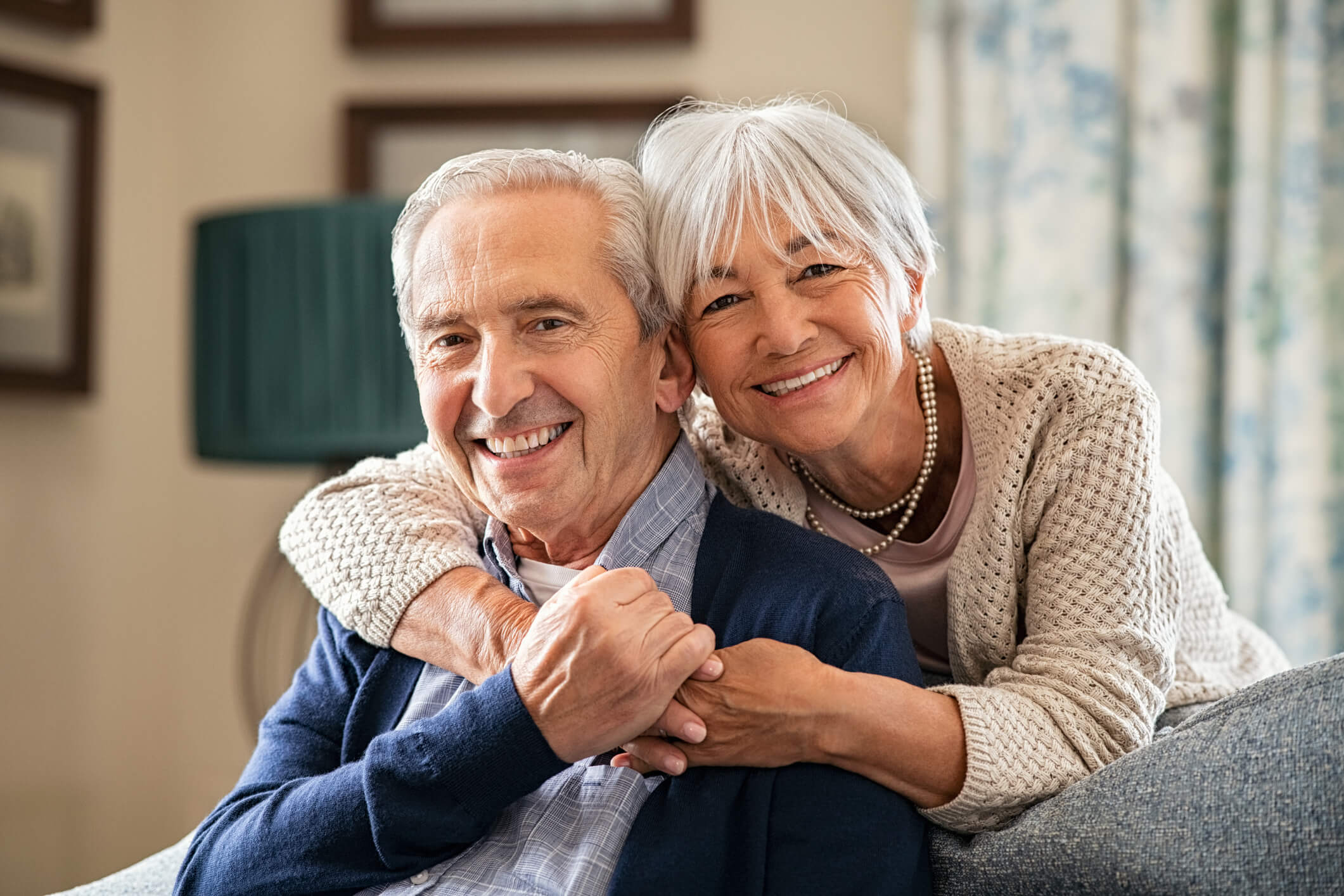 Elderly couple smiling side by side while sitting down.